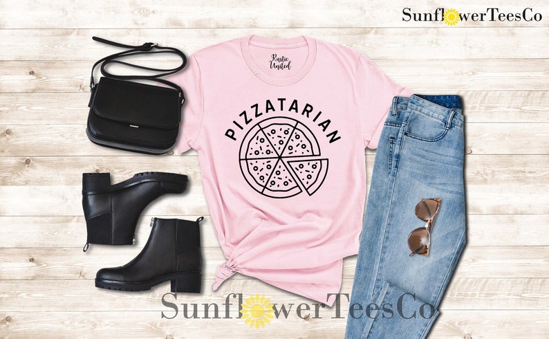 May include: Pink t-shirt with the text "Pizzatarian" and a black and white illustration of a pizza slice. The shirt is paired with blue jeans, black boots, and a black purse.