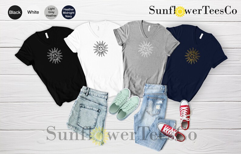May include: Four V-neck t-shirts with a graphic of a sun on the front. The shirts are in black, white, heather grey, and midnight navy. The shirts are laid out on a wooden surface with a pair of blue jeans and a pair of white sneakers.
