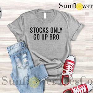 May include: A light grey heather t-shirt with the text "STOCKS ONLY GO UP BRO" printed in black.