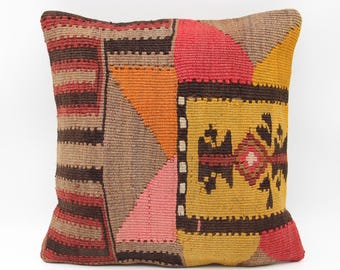 May include: Square decorative pillow with a patchwork design. The pillow features a mix of colors including brown, red, orange, pink, and yellow. The pillow has a geometric pattern with a central floral motif.