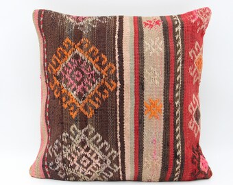 May include: Square decorative pillow with a woven design. The pillow features a brown background with orange, pink, and beige geometric patterns and stripes. The edges are trimmed with a pink border. This pillow is a great addition to any home decor.