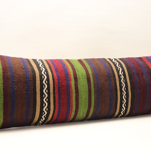 Puede incluir: Una almohada larga y rectangular con un patrón de rayas en tonos de marrón, verde, rojo, azul y beige. La almohada está hecha de tejido tejido y tiene una superficie ligeramente texturizada.