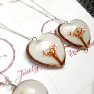 Puede incluir: Collares de resina en forma de coraz&oacute;n y redondos con cadenas de plata. Los colgantes de coraz&oacute;n contienen un dise&ntilde;o marr&oacute;n y dorado con detalles en rojo. El colgante redondo tiene un remolino de cabello casta&ntilde;o.