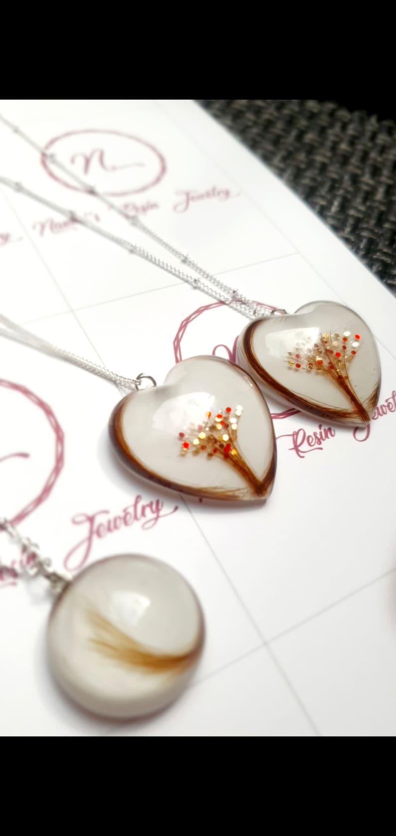 Puede incluir: Collares de resina en forma de coraz&oacute;n y redondos con cadenas de plata. Los colgantes de coraz&oacute;n contienen un dise&ntilde;o marr&oacute;n y dorado con detalles en rojo. El colgante redondo tiene un remolino de cabello casta&ntilde;o.