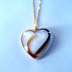 Puede incluir: Collar con colgante en forma de coraz&oacute;n y cadena dorada. El colgante transparente contiene mechones de cabello casta&ntilde;o y negro. Una joya delicada.