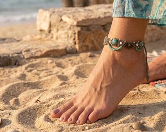 May include: An anklet featuring a woven cord design with small turquoise-colored beads and metallic accents. The jewelry piece is constructed with a series of interconnected loops and decorative elements that wrap around the ankle area.