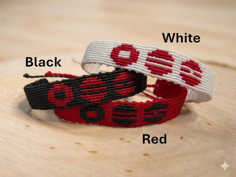 Puede incluir: Tres pulseras de amistad tejidas en negro, rojo y blanco. Cada pulsera presenta un patr&oacute;n repetitivo de c&iacute;rculos rojos. Las pulseras est&aacute;n apiladas sobre una superficie de madera. Las palabras "White", "Black" y "Red" est&aacute;n escritas en la imagen.