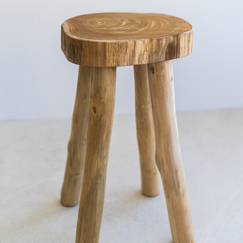 May include: A wooden stool with a natural wood finish and four legs. The top of the stool is a thick slice of wood with a natural grain pattern.