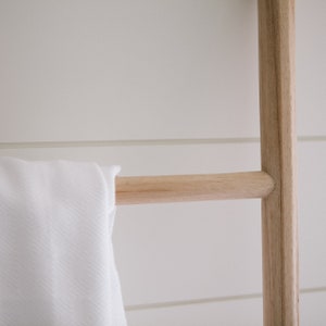 Puede incluir: Una toalla blanca cuelga de un estante de escalera de madera. La escalera est&aacute; hecha de madera natural y tiene un aspecto r&uacute;stico.