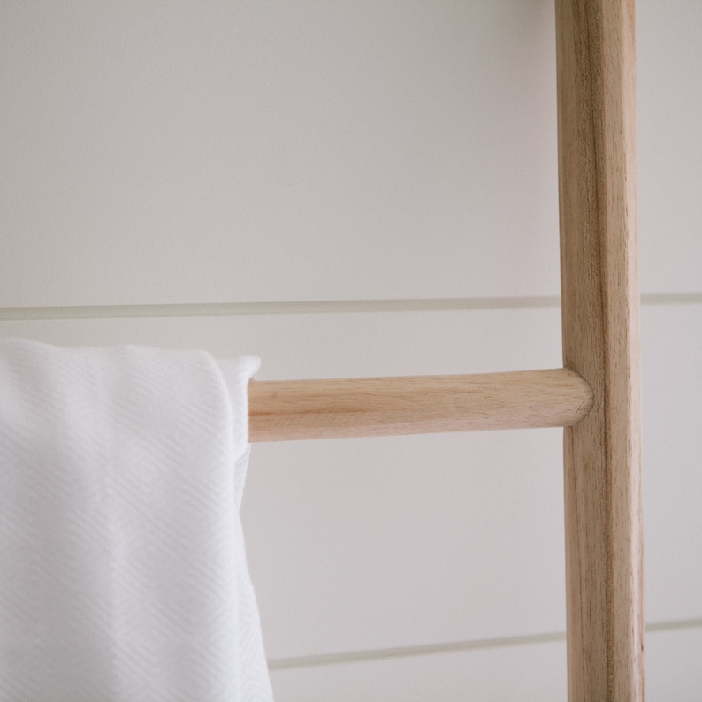 Puede incluir: Una toalla blanca cuelga de un estante de escalera de madera. La escalera est&aacute; hecha de madera natural y tiene un aspecto r&uacute;stico.