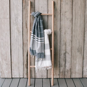 Puede incluir: Dos toallas rayadas colgadas de una escalera de madera sobre un fondo de panel de madera. Una toalla es blanca con rayas negras y la otra es gris oscuro con rayas blancas.