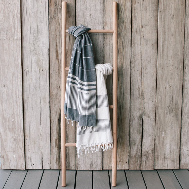 Puede incluir: Dos toallas rayadas colgadas de una escalera de madera sobre un fondo de panel de madera. Una toalla es blanca con rayas negras y la otra es gris oscuro con rayas blancas.