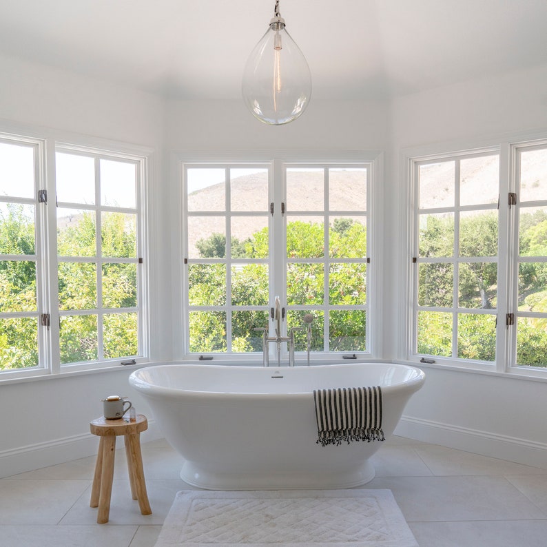 teak stool with coffee mug and crystal point in a bathroom with a free-standing tub and black and white stripped turkish towel