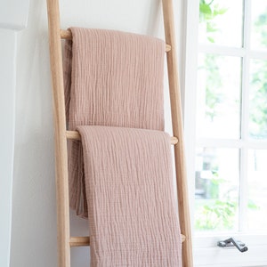 Puede incluir: Una escalera de madera con dos mantas rosas dobladas y drapeadas sobre ella. Las mantas tienen un ribete de flecos.