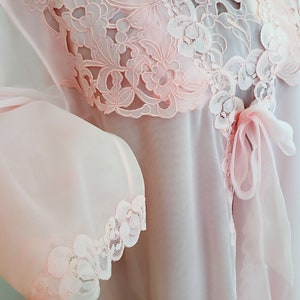 May include: A delicate pink sheer robe with lace trim and a bow at the waist.