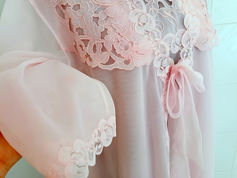 May include: A delicate pink sheer robe with lace trim and a bow at the waist.