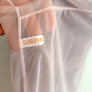 May include: A pale pink sheer fabric with a white label that reads "BIANCHERI".