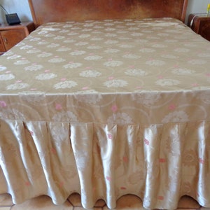 May include: A gold bed skirt with a pink floral pattern. The skirt has a ruffled edge and is made of a silky fabric.