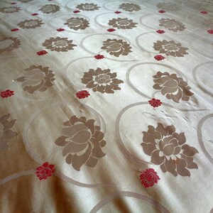 May include: A close-up of a beige fabric with a repeating pattern of brown lotus flowers and small red flowers.