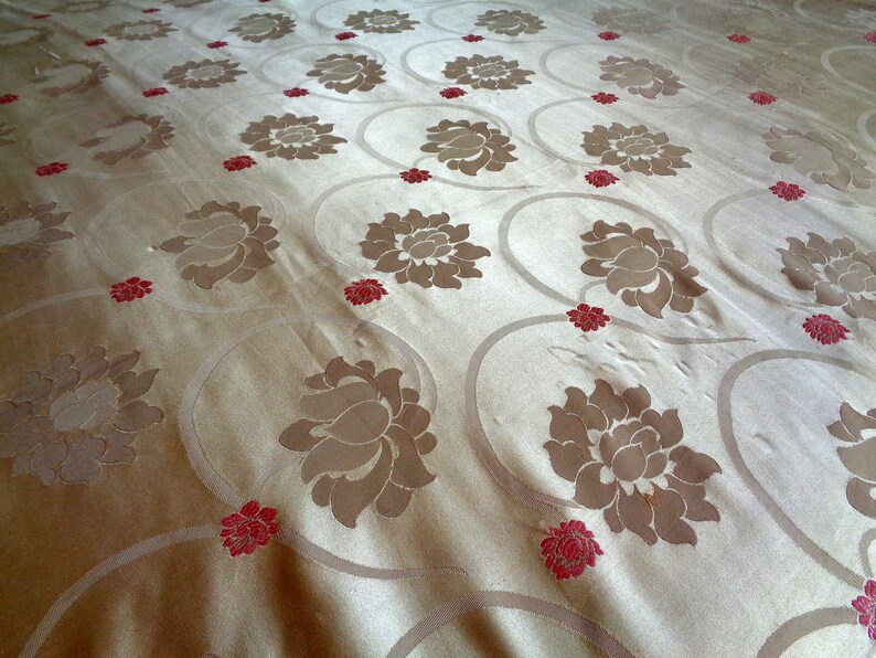 May include: A close-up of a beige fabric with a repeating pattern of brown lotus flowers and small red flowers.