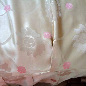 May include: A close-up of a cream-colored fabric with a floral pattern. The fabric has a subtle sheen and is decorated with pink flowers.
