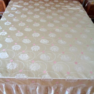 May include: A gold bedspread with a white floral pattern and pink accents. The bedspread has a ruffled edge.
