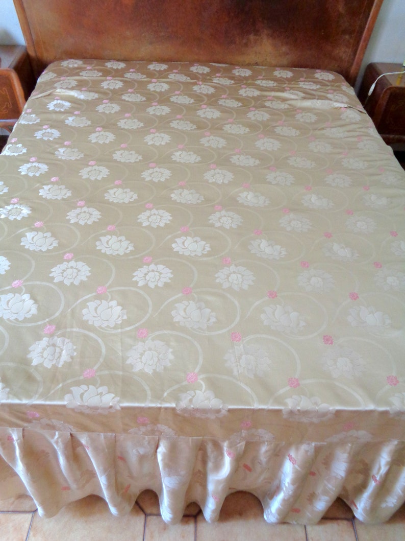 May include: A gold bedspread with a white floral pattern and pink accents. The bedspread has a ruffled edge.