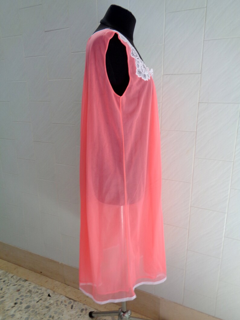 May include: A pink sheer nightgown with a white lace trim around the neckline. The gown is sleeveless and has a flowing silhouette.