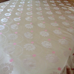 May include: A white bedspread with a delicate floral pattern in pink. The bedspread has a ruffled edge.