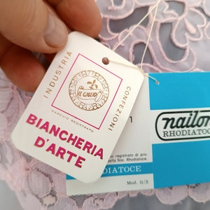 May include: A white tag with the text "INDUSTRIA BIANCHERIA D'ARTE" and a logo of a flower with the text "IL GIGLIO" and "MARCHIO REGISTRATO". A blue tag with the text "nailon RHODIATOCE" and "Mod. 11/3".