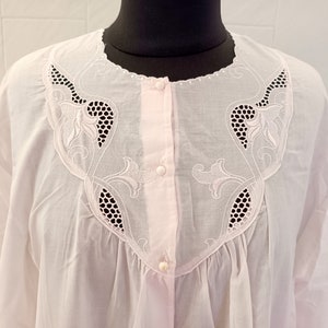 Peut inclure: Une chemise de nuit en coton blanc avec une délicate bordure en dentelle rose et un devant boutonné. La dentelle présente un motif floral.