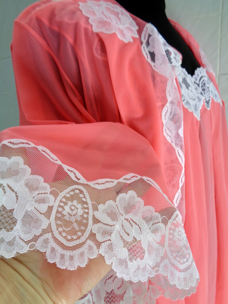 May include: A pink sheer nightgown with white lace trim. The lace features a floral design.