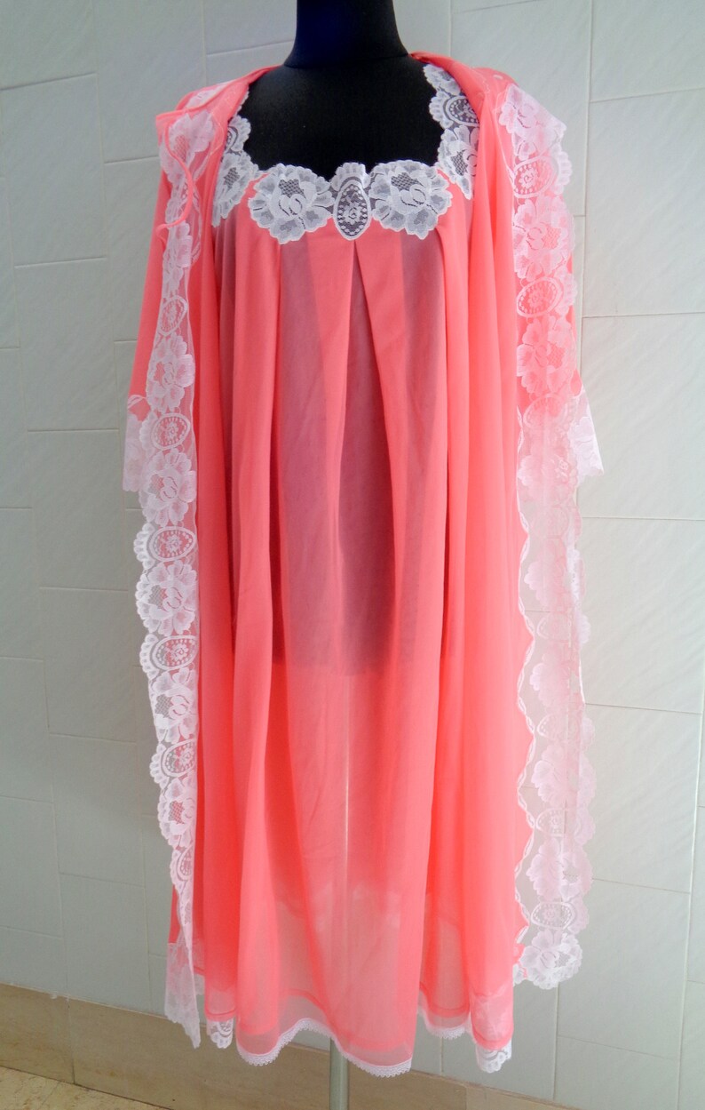 May include: A pink sheer nightgown with white lace trim. The gown has a scoop neck and is made of a lightweight fabric.