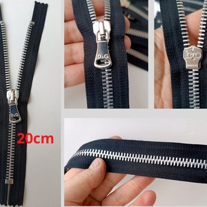 May include: A black zipper with silver teeth and a silver pull tab. The pull tab has the text "D.G." on it. The zipper is 20 inches long.