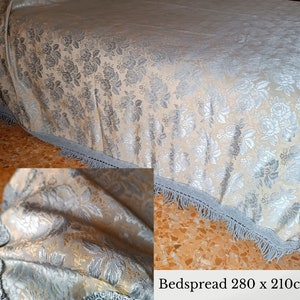 May include: A bedspread with a floral design in silver and gold hues. It features a light blue fringe trim. The dimensions are 280 x 210cm, equivalent to approximately 110 x 83 inches. The text on the image reads 'Bedspread 280 x 210cm'.
