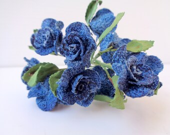 Pode incluir: Um buquê de rosas de brim azul com folhas verdes. As rosas são feitas de tecido e têm uma superfície texturizada.