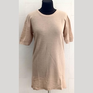 May include: A beige short-sleeved t-shirt displayed on a black mannequin. The shirt has a crew neck and a relaxed fit. The fabric appears to be a soft, textured material.