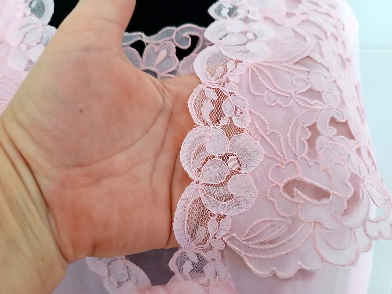 May include: Pink lace fabric with a floral design. The lace is delicate and intricate, with a scalloped edge.