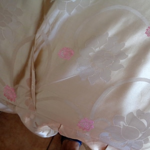 May include: A close-up of a beige fabric with a floral pattern. The fabric has a subtle sheen and is decorated with pink flowers.
