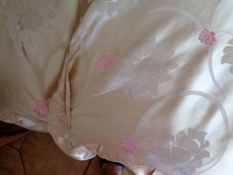 May include: A close-up of a beige fabric with a floral pattern. The fabric has a subtle sheen and is decorated with pink flowers.