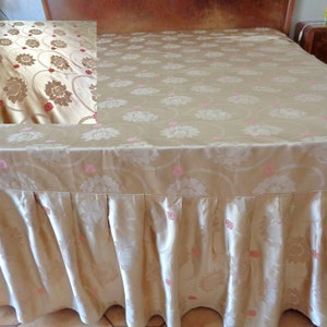 May include: A gold bed skirt with a floral pattern and pink accents. The skirt is made of a soft, silky fabric and has a ruffled edge.