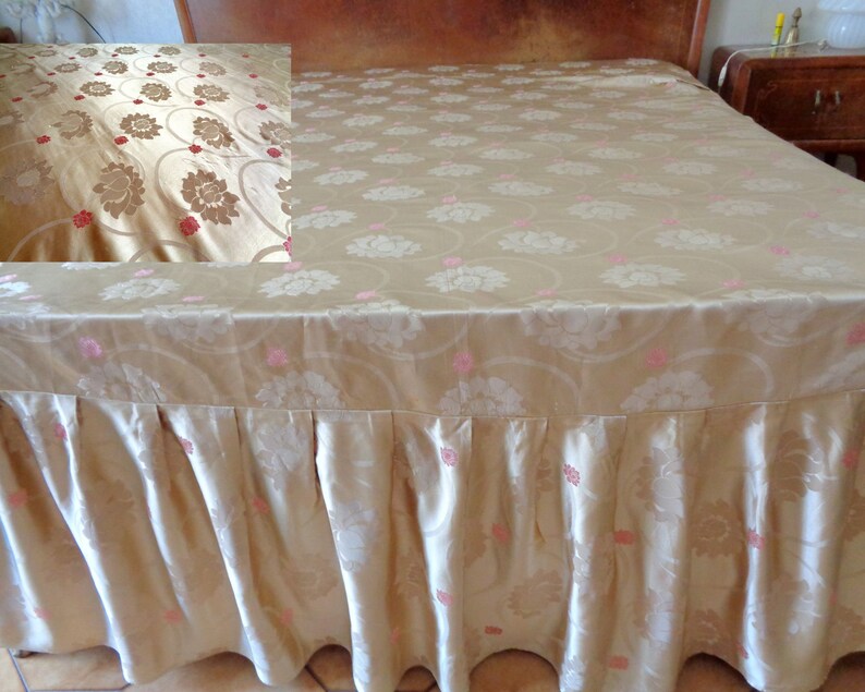 May include: A gold bed skirt with a floral pattern and pink accents. The skirt is made of a soft, silky fabric and has a ruffled edge.