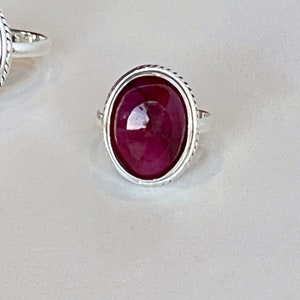 May include: A silver ring with a large oval-shaped, deep red gemstone set in a silver bezel.