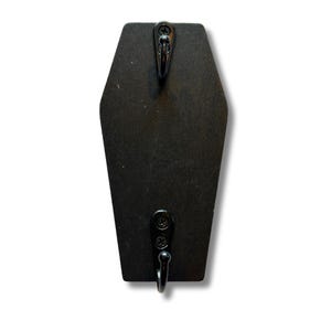 以下が含まれることがあります： 黒い棺型のウォールフック。2つの黒い金属製のフックとネジが付いています。フックは木製で、物を吊るすように設計されています。デザインはシンプルでゴシック様式で、さまざまな装飾スタイルに適しています。