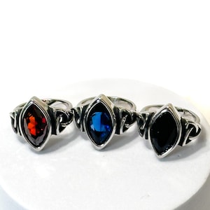 May include: Three silver rings with different colored gemstones. The rings have a detailed design with a marquise-shaped stone in the center. The stones are red, blue, and black.
