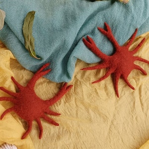 Pode incluir: Uma coleção de criaturas marinhas de feltro feitas à mão, incluindo um polvo vermelho, uma água-viva rosa, um peixe amarelo e duas estrelas do mar vermelhas, dispostas sobre um fundo de tecido azul e amarelo. Os animais de feltro são detalhados e caprichosos.