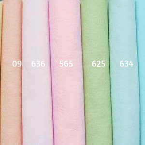 May include: A collection of fabric rolls in various pastel colors, including white, yellow, peach, pink, green, and blue. Each roll is labeled with a number. The fabrics appear soft and textured, suitable for crafts or decorative projects.