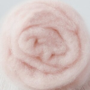 May include: A close-up of a soft, fluffy, pale pink wool roving. The wool is tightly packed together, creating a smooth, even surface.