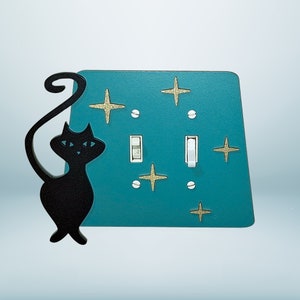 May include: A teal blue light switch cover with a black silhouette of a cat and gold star accents.