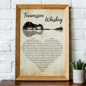 May include: A framed print with the words "Tennessee Whiskey" at the top. The print features a silhouette of trees and a body of water. The lyrics of the song are printed below the image in a stylized font.